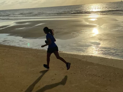 Femme courant sur plage au coucher du soleil.