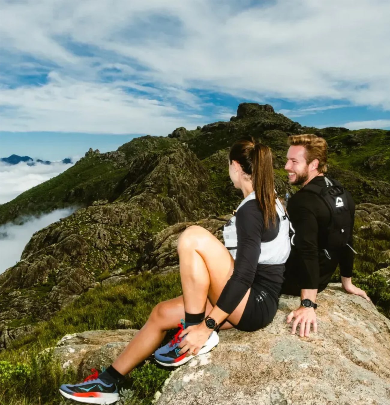 Couple assis sur rocher, vue montagneuse.