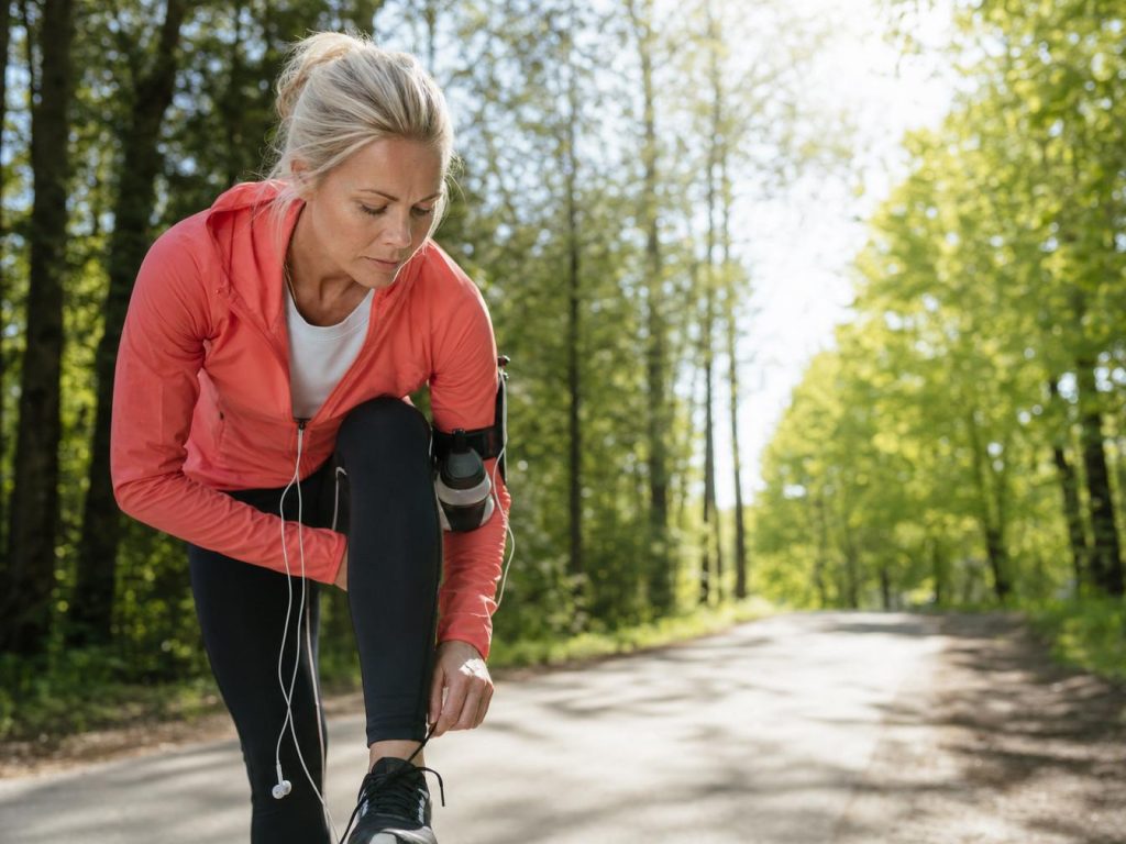 Coureuse s'arretant sur un sentier pour verifier une blessure au genou, marathon