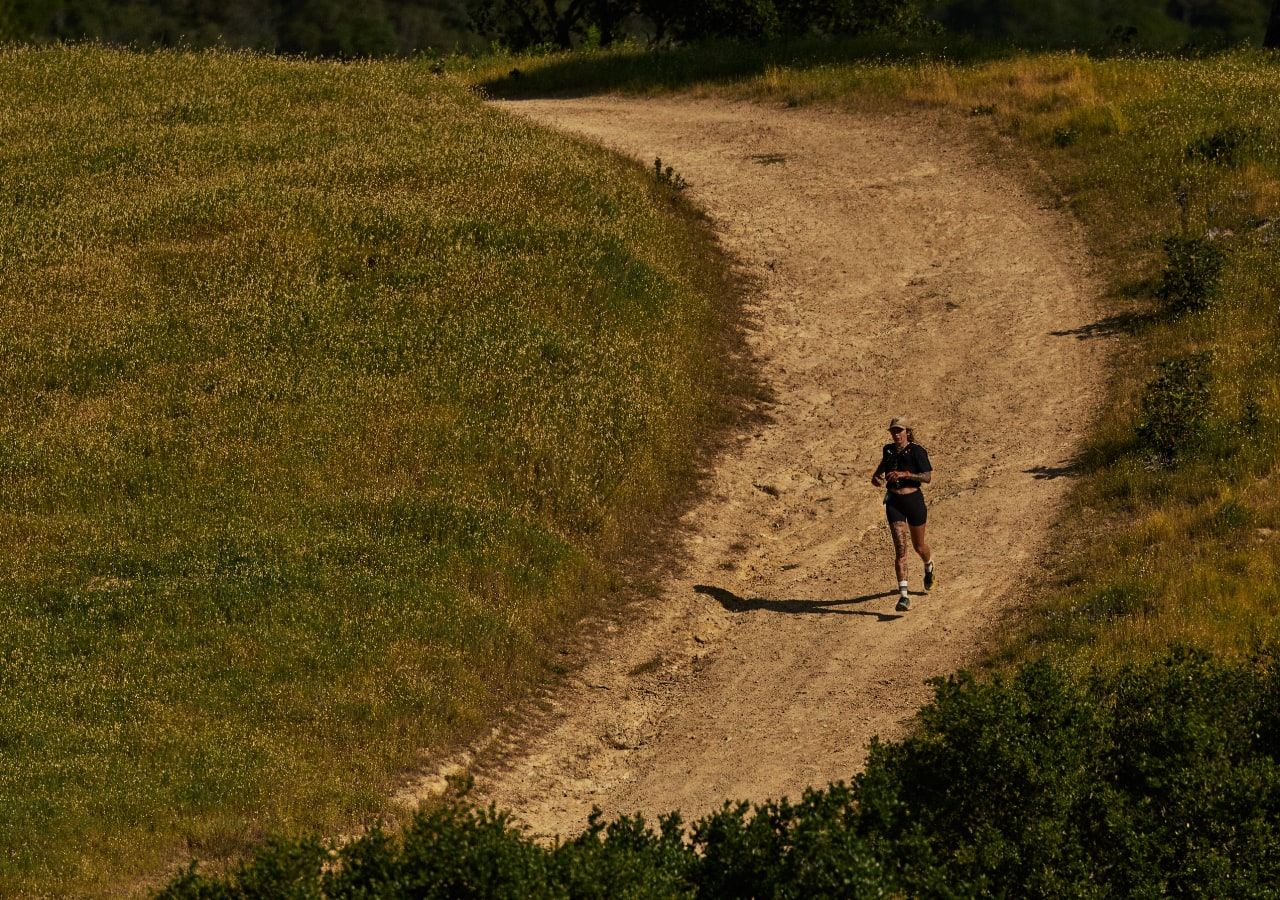 Coureuse sur sentier poussiéreux au milieu des collines