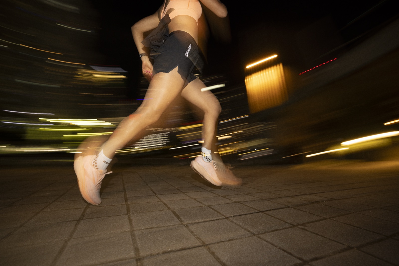 Coureuse en Brooks Ghost Amp lancée de nuit sur un trottoir éclairé